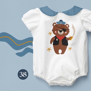 May include: White baby onesie with a blue collar and a brown bear wearing a pirate hat and eyepatch. The bear is holding a sword and has a skull and crossbones on its vest. The onesie has a number 38 on the bottom left corner.