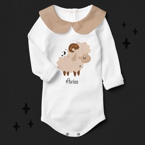 Pode incluir: Macac&atilde;o branco de manga comprida para beb&ecirc; com gola marrom e um carneiro de desenho animado marrom e branco com o texto "Aries" embaixo.