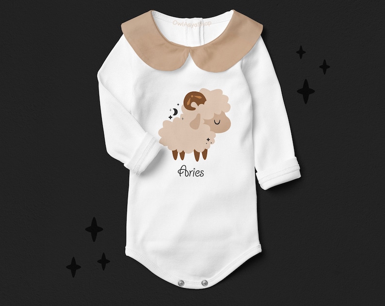 Pode incluir: Macac&atilde;o branco de manga comprida para beb&ecirc; com gola marrom e um carneiro de desenho animado marrom e branco com o texto "Aries" embaixo.