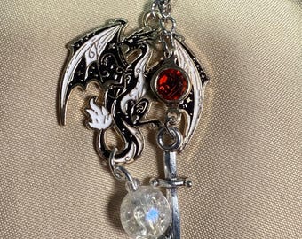 May include: A silver charm with a black and white dragon design, a red gemstone, a silver sword, and a clear crystal bead.