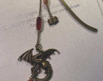May include: A bronze dragon bookmark with a red gemstone, a small book charm, and two amber-colored beads. The bookmark is attached to a chain and has a bronze metal tab.