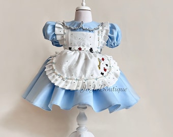 Könnte beinhalten: Ein hellblaues Kleid mit kurzen Puffärmeln und einer weißen Schürze mit gerüschtem Rand. Die Schürze ist mit kleinen roten und schwarzen Spielkartensymbolen und einem goldenen Schlüssel verziert. Der Text JoJoBoutique ist auf dem Rock sichtbar.