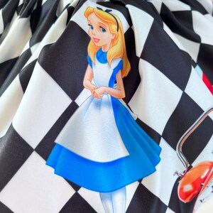 May include: Alice in Wonderland themed fabric with a black and white checkered pattern. The fabric features a cartoon image of Alice in her blue dress, standing on the checkered pattern. The fabric also features a red teapot and a white rabbit.