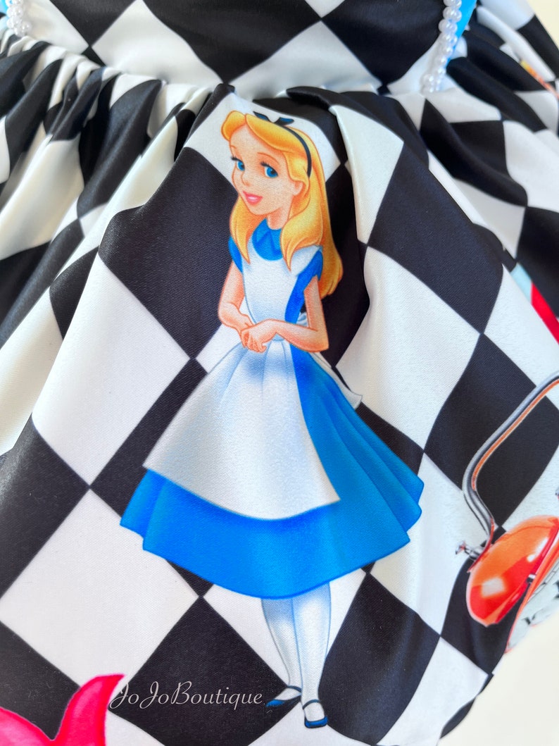 May include: Alice in Wonderland themed fabric with a black and white checkered pattern. The fabric features a cartoon image of Alice in her blue dress, standing on the checkered pattern. The fabric also features a red teapot and a white rabbit.