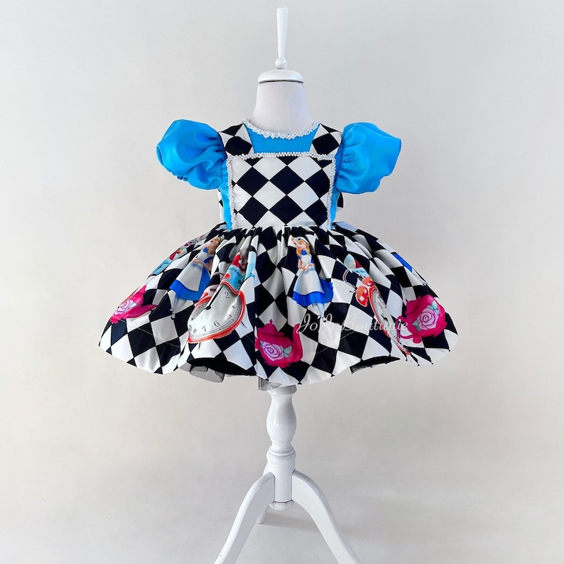 May include: A black and white checkered dress with a blue bodice and puff sleeves. The dress features Alice in Wonderland characters and a pocket watch.