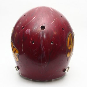 K&ouml;nnte beinhalten: Ein dunkelroter Footballhelm mit einem gelben und goldenen Logo, auf dem "YHS" steht. Der Helm hat mehrere kleine L&ouml;cher und weist Gebrauchsspuren auf.