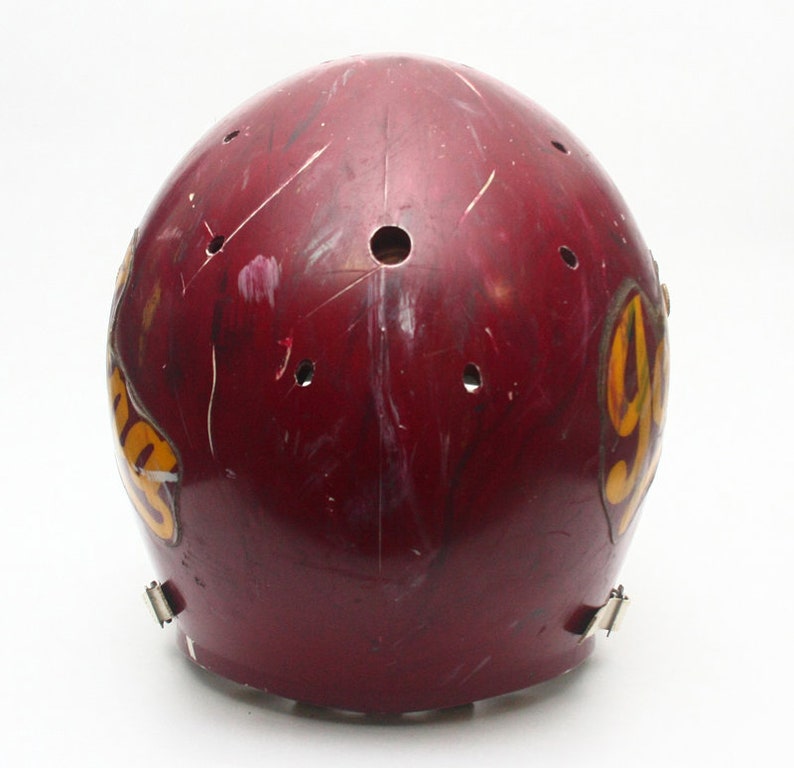 K&ouml;nnte beinhalten: Ein dunkelroter Footballhelm mit einem gelben und goldenen Logo, auf dem "YHS" steht. Der Helm hat mehrere kleine L&ouml;cher und weist Gebrauchsspuren auf.