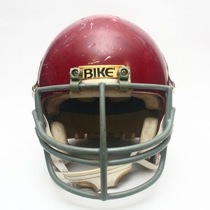 K&ouml;nnte beinhalten: Ein roter Footballhelm mit einem grauen Gesichtsgitter und einem gelben Aufkleber mit der Aufschrift "BIKE".