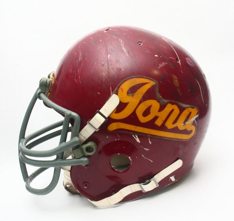 K&ouml;nnte beinhalten: Ein maroonfarbener Footballhelm mit einem grauen Gesichtsgitter und einem goldenen "Iona"-Logo.