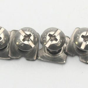 Puede incluir: Cuatro tornillos plateados con bases cuadradas y cabeza en forma de cruz. Cada tornillo tiene el texto "SOCKET HEAD" y "USA" impreso en la cabeza.
