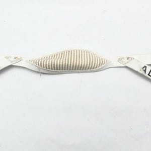 Puede incluir: Casco de cuero blanco con una sección central acolchada y correas ajustables. Las correas tienen hebillas metálicas y el nombre "ADAM" y el número "95" impresos. La sección acolchada tiene un patrón de rayas.