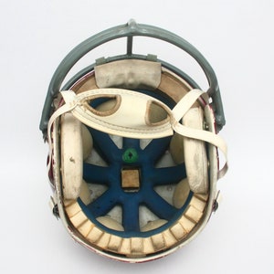 K&ouml;nnte beinhalten: Ein Vintage-Footballhelm mit rot-wei&szlig; gestreiftem &Auml;u&szlig;eren. Der Helm hat ein graues Metallgesichtsschutzgitter und ein wei&szlig;es Lederinnere mit Polsterung.