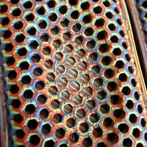 May include: Close-up of a pair of colorful insoles with a honeycomb pattern. The insoles feature a vibrant gradient of colors, including red, blue, and yellow. The design incorporates numerous circular openings for breathability and comfort.