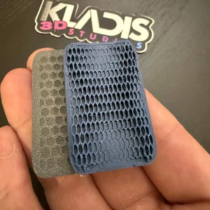 以下が含まれることがあります： ハニカム模様の2つの3Dプリントされた長方形のオブジェクト。1つはグレー、もう1つはブルーです。オブジェクトは手で持たれています。「KLADIS 3D STUDIOS」というテキストのステッカーが背景にあります。