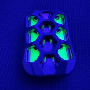 May include: A black, rectangular device with a honeycomb design, illuminated by a bright green glow. The text "T48" is visible. The device is set against a dark blue background.