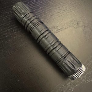 May include: A black, cylindrical, textured object with a silver cap on one end. The object is made of a hard material and has a smooth, glossy finish.
