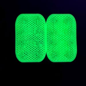 以下が含まれることがあります： 角が丸い2つの長方形のオブジェクト。明るいネオングリーンの光を放ち、均一なハニカム格子構造をしています。表面には小さな六角形の穴が等間隔に開いており、格子状のテクスチャが形成されています。