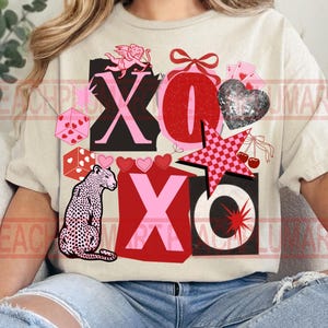 May include: Beige t-shirt with a graphic design featuring the letters X and O, hearts, dice, a leopard, a star, and cherries. The design incorporates pink, red, black, and white elements, creating a playful and romantic aesthetic.