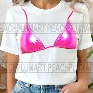 Op de afbeelding: Wit T-shirt met een felroze bikini top ontwerp. De afbeelding heeft een glanzende, reflecterende uitstraling met een contrasterende omtrek. Dit casual T-shirt is geschikt voor zomerse of strandgerelateerde evenementen.