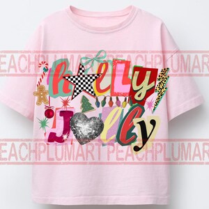 K&ouml;nnte beinhalten: Ein hellrosa T-Shirt mit dem Schriftzug "Holly Jolly" in einem farbenfrohen Design im Collage-Stil. Das Design umfasst einen karierten Stern, ein paillettenbesetztes Herz und weihnachtliche Grafiken.