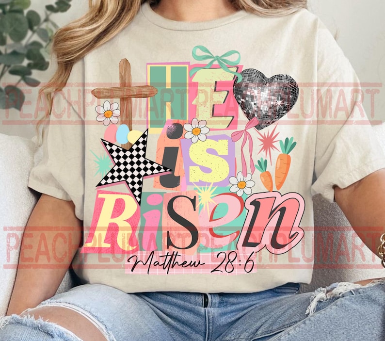 May include: Cream-colored t-shirt with a colorful graphic that reads "He is Risen" with a cross, star, heart, flowers, and carrots. The text "Matthew 28:6" is below the main text. The design has a pastel color scheme.