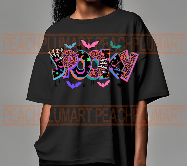 Puede incluir: Camiseta negra con un dise&ntilde;o gr&aacute;fico colorido que dice "Spooky" con murci&eacute;lagos, estrellas y detalles de estampado de leopardo.