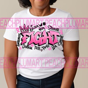 Op de afbeelding: Wit T-shirt met een roze grafisch ontwerp met de tekst "FIGHT" in grote letters. De grafiek bevat ook de woorden "Awareness", "Believe", "Hope", "Strength", "Courage", "Faith", "Family", "Love" en "Support".