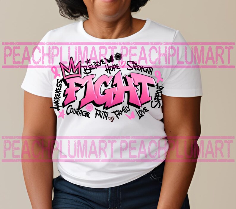 Op de afbeelding: Wit T-shirt met een roze grafisch ontwerp met de tekst "FIGHT" in grote letters. De grafiek bevat ook de woorden "Awareness", "Believe", "Hope", "Strength", "Courage", "Faith", "Family", "Love" en "Support".