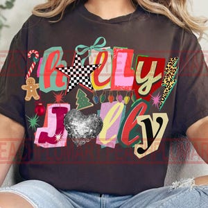 K&ouml;nnte beinhalten: Ein dunkelbraunes T-Shirt mit dem Schriftzug "Holly Jolly" in einem farbenfrohen, festlichen Design. Das Design umfasst einen Lebkuchenmann, eine Zuckerstange, ein Discokugelherz und einen karierten Stern, ideal f&uuml;r die Weihnachtszeit.
