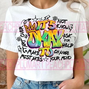 Puede incluir: Camiseta blanca con un diseño colorido estilo grafiti. El diseño incluye las palabras "IT'S OKAY TO MAKE MISTAKES" en letras grandes y vibrantes, junto con otras frases y gráficos. Un artículo casual para el uso diario.