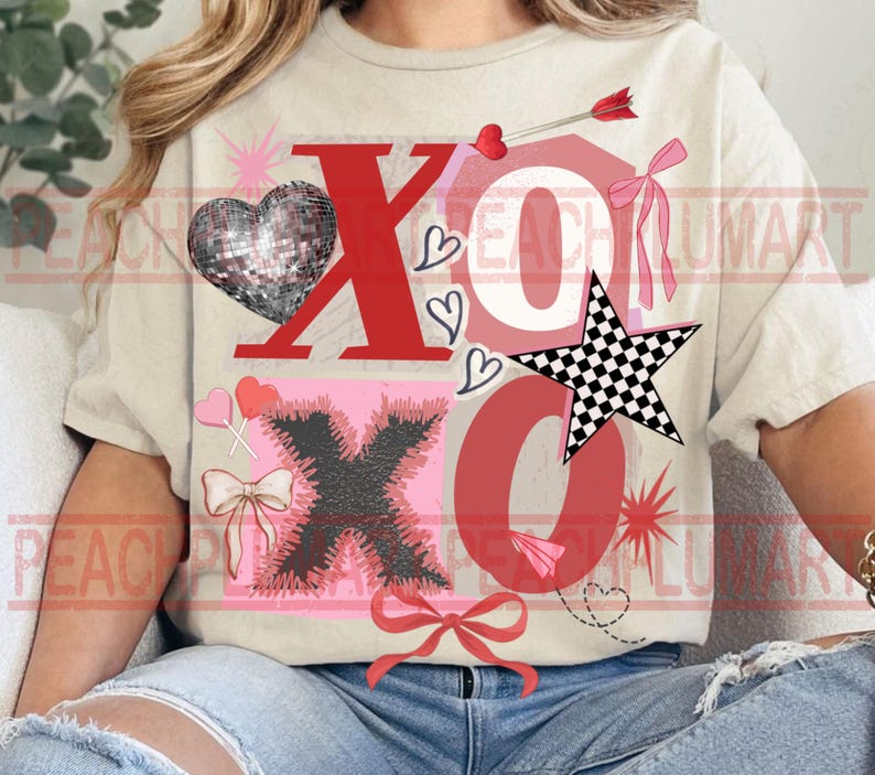 May include: A beige t-shirt with a Valentine's Day design. The design includes the letters "XO" in red and black, a disco ball heart, a checkered star, hearts, bows, and an arrow. The shirt is a casual, everyday wear item.
