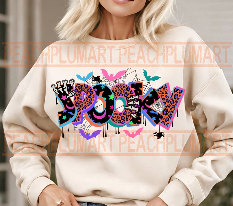 Puede incluir: Una sudadera de color crema con un dise&ntilde;o gr&aacute;fico colorido que dice "Spooky" en una fuente que gotea. El gr&aacute;fico incluye murci&eacute;lagos, ara&ntilde;as, estrellas y un estampado de leopardo.