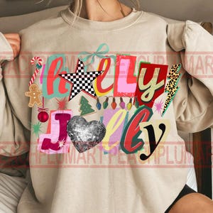 K&ouml;nnte beinhalten: Beiges Sweatshirt mit einem farbenfrohen &bdquo;Holly Jolly&ldquo;-Grafikdesign. Das Design umfasst einen karierten Stern, ein Discokugelherz, einen Weihnachtsbaum, eine Zuckerstange und andere festliche Elemente. Ein fr&ouml;hliches, weihnachtliches Oberteil.