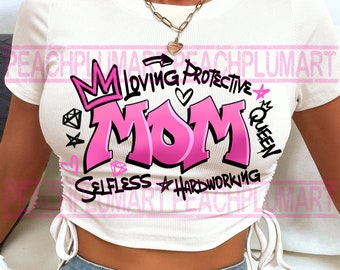 May include: White crop top with a pink graphic that says "Mom" in graffiti style lettering. The graphic also includes a crown, hearts, stars, and the words "Loving, Protective, Queen, Selfless, Hardworking".
