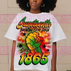 May include: White t-shirt with a graphic design featuring a raised fist, stars, and the text "Juneteenth Breaking Every Chain Since 1865". The graphic is in shades of green, yellow, red, and black.