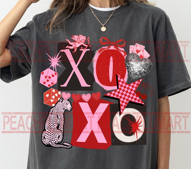 May include: Dark gray t-shirt with a graphic design featuring the letters "XO", a leopard, dice, hearts, a disco ball heart, and a star. The design incorporates pink, red, and white elements.