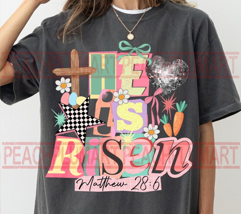 May include: Dark gray t-shirt with a colorful graphic design. The design includes a wooden cross, a disco ball heart, and the words "He Has Risen" with the Bible verse Matthew 28:6.