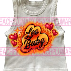 May include: White ribbed tank top with an airbrushed design. The design features the words "Leo Baby" in black script, surrounded by orange flames, stars, and red hearts. The tank top is sleeveless.