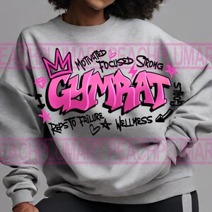 Op de afbeelding: Grijs sweatshirt met een roze grafisch ontwerp met de tekst "GYMBAT" met de woorden "Motivated", "Focused", "Strong", "Reps to Failure", "Wellness" en "Goals" eromheen.
