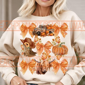 Op de afbeelding: Een crèmekleurige trui met een herfstthema-ontwerp met een vintage vrachtwagen met pompoenen, een hooglandkoe, cowboylaarzen en strikken met herfstbladeren.
