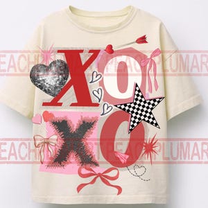May include: Cream-colored t-shirt with a graphic design featuring the letters "XO" in red and black, along with a disco ball heart, a checkered star, and bows. The design includes hearts and an arrow.