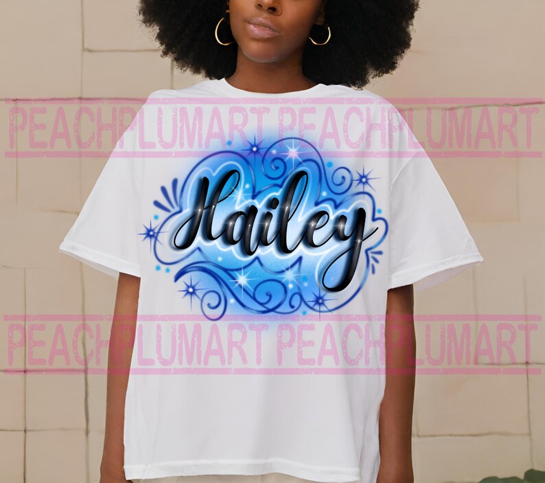 Peut inclure: T-shirt blanc avec un motif a&eacute;rographe bleu et noir repr&eacute;sentant le nom "Hailey" dans une police stylis&eacute;e avec des volutes et des &eacute;toiles.