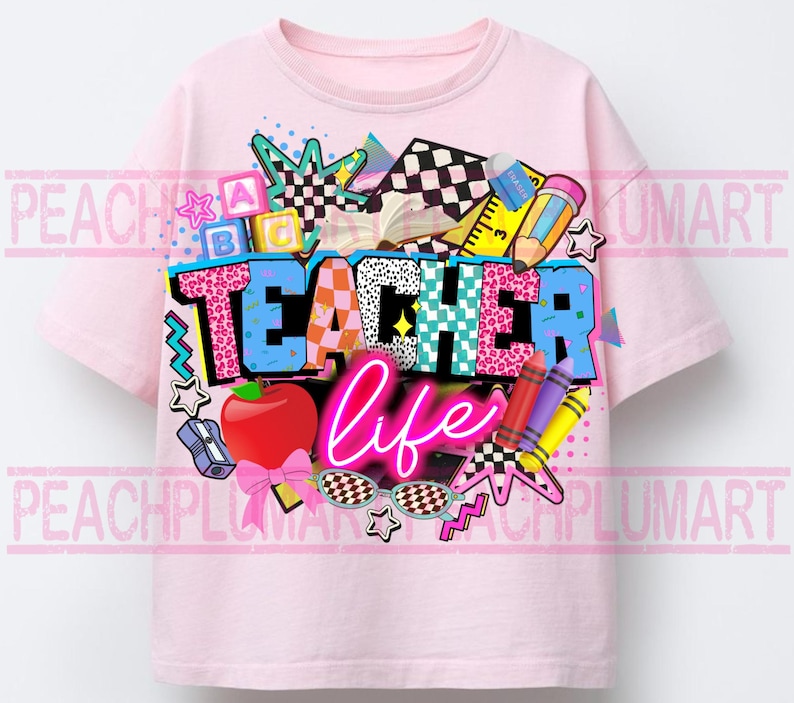 May include: A light pink t-shirt with a colorful graphic design. The design features the words "TEACHER life" in a mix of fonts and patterns, along with school-themed elements like an apple, pencils, and sunglasses. The shirt is a crew neck style.
