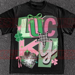 May include: Black t-shirt with a graphic design that says "LUCKY" in green, pink, and white. The design includes a four-leaf clover, a disco ball heart, and a checkered star.