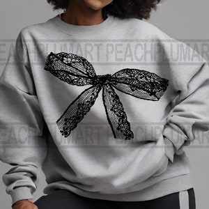 K&ouml;nnte beinhalten: Ein grauer Pullover mit einem schwarzen Spitzenbogen auf der Vorderseite.