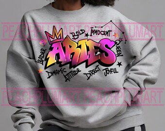 Könnte beinhalten: Grauer Pullover mit einem pinkfarbenen und gelben Graffiti-Design, das "Aries" mit einer Krone und einem Diamanten über dem Wort sagt. Das Design ist umgeben von Wörtern wie "leader", "bold", "innocent", "dynamic", "attitude", "direct" und "joyful".