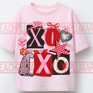 May include: A light pink t-shirt featuring a graphic print with the text XOXO, a leopard, a silver glitter heart, a red bow, a pink checkered star, dice, cherries, and a cupid. The design includes various red, pink, and black elements.