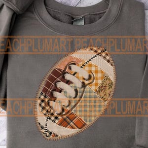 May include: Gray sweatshirt with a football-shaped patch. The patch is made of various fabric patterns in shades of brown, orange, and cream, with the word "Fall" stitched in white.