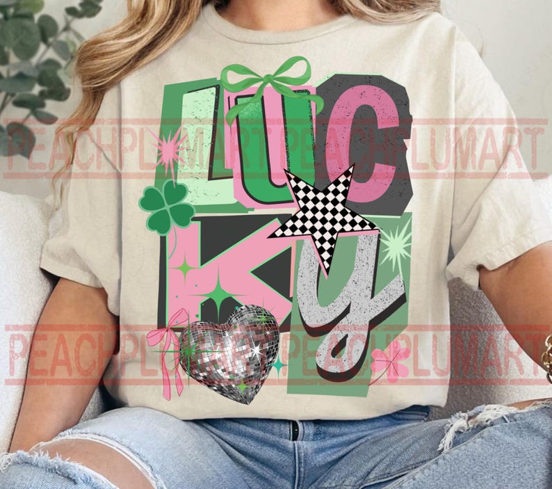 May include: Cream-colored t-shirt with the word "LUCKY" in a colorful design. The design includes a four-leaf clover, a checkered star, a disco ball heart, and bows. The letters are in green, pink, and gray.