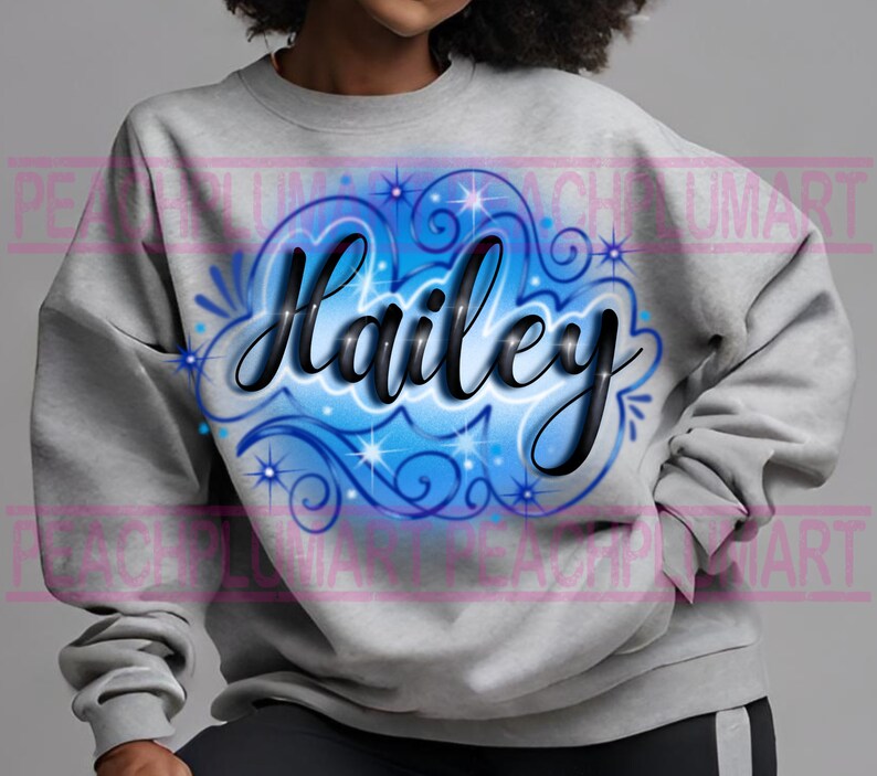Peut inclure: Un sweat-shirt gris avec un motif a&eacute;rographe bleu et blanc repr&eacute;sentant le nom "Hailey" en lettres cursives noires.
